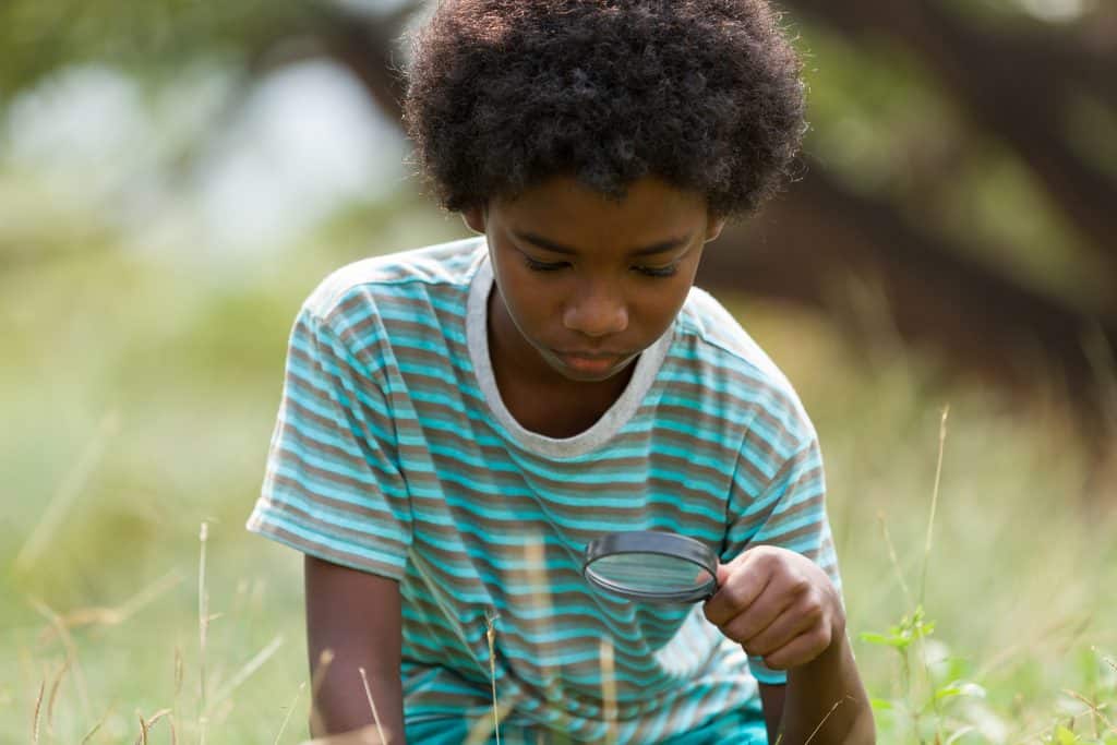 Child examining plants with a magnifying glass outdoors for peace and unity.