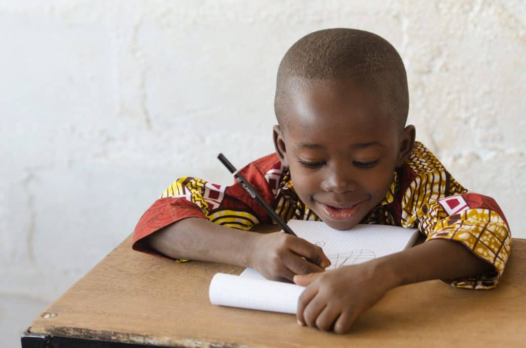 Young boy writing in a notebook at a wooden desk.