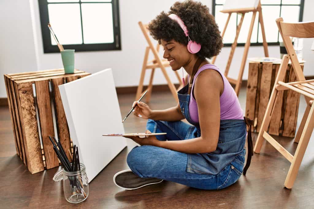 Young woman painting on canvas in art studio with headphones and natural light.
