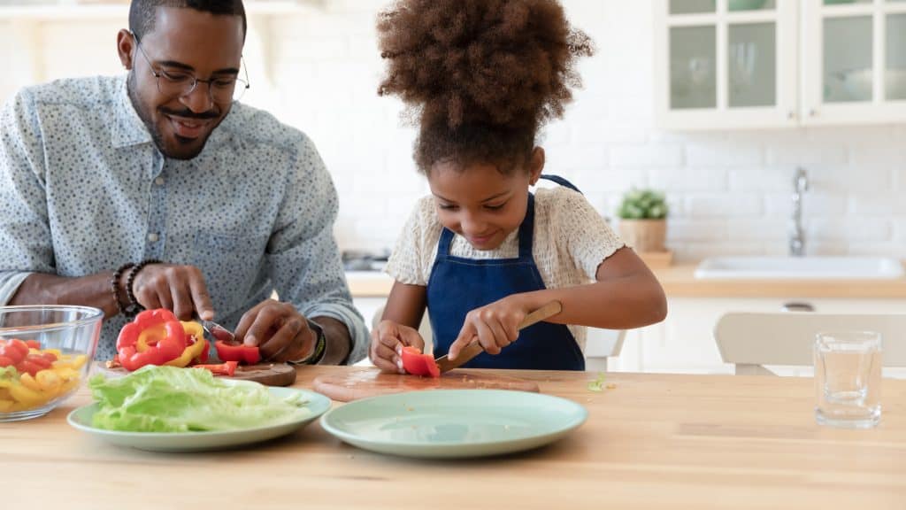 Father and daughter preparing vegetables in a bright kitchen.